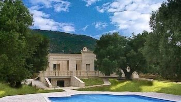 A large swimming pool with a stone deck, surrounded by lush greenery and a large building in the background. - La Vigna Vecchia (Fasano)