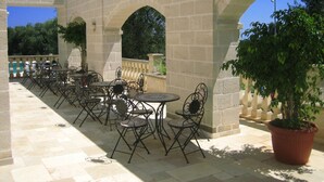 An outdoor patio with stone arches, tables, and chairs, surrounded by potted plants. - La Vigna Vecchia (Fasano)