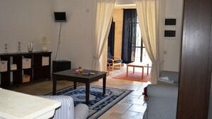A living room with a sofa, a coffee table, a TV, and a bookshelf. There is a window with curtains and a door leading to another room. - La Vigna Vecchia (Fasano)