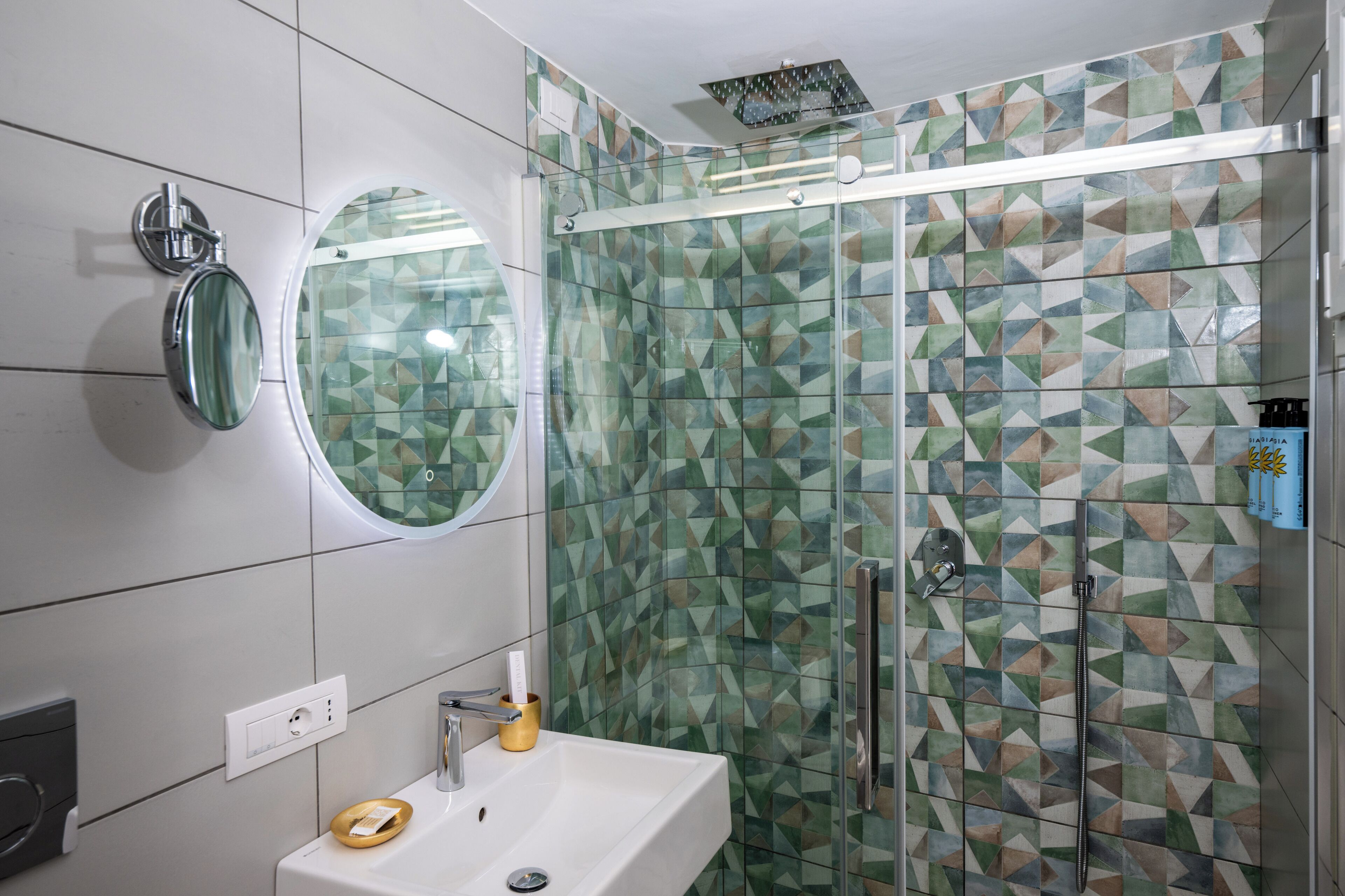 A bathroom with a sink, mirror, and shower with geometric patterned tiles.