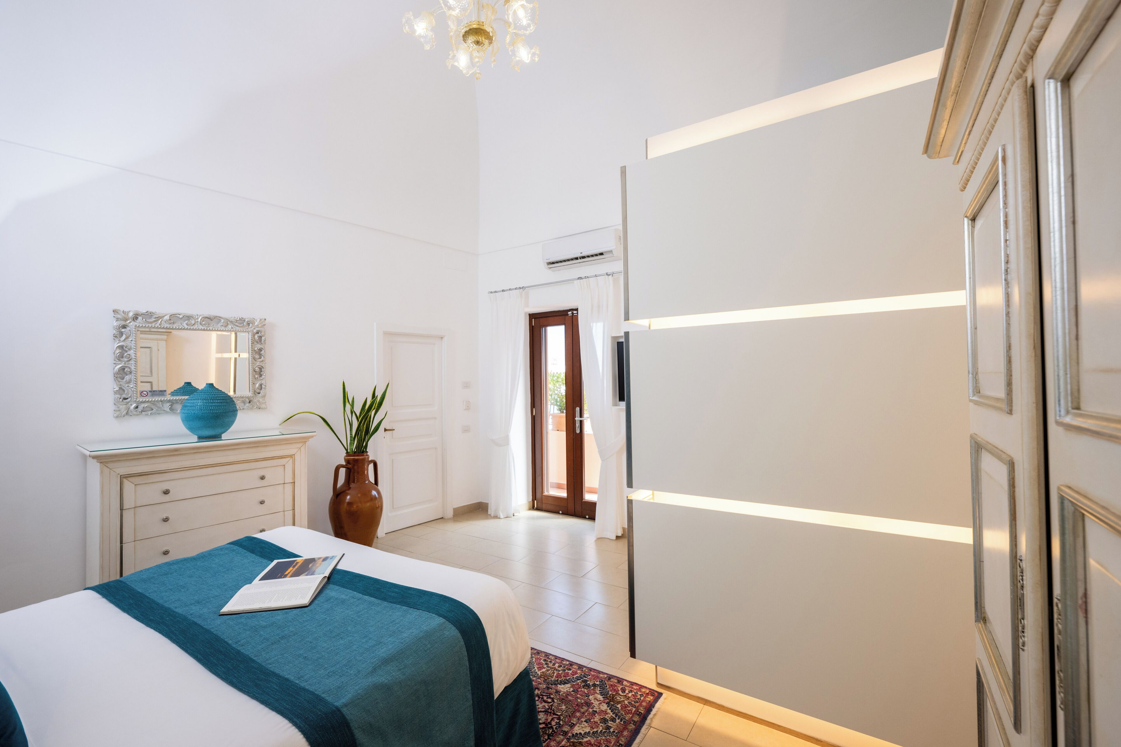 Un dormitorio con cama, cómoda, espejo y una puerta que da a otra habitación.