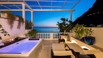 A rooftop terrace with a hot tub, seating area, and potted plants.