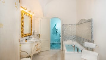 A bathroom with a marble sink, a large mirror with a gold frame, a bathtub, and a shower area.