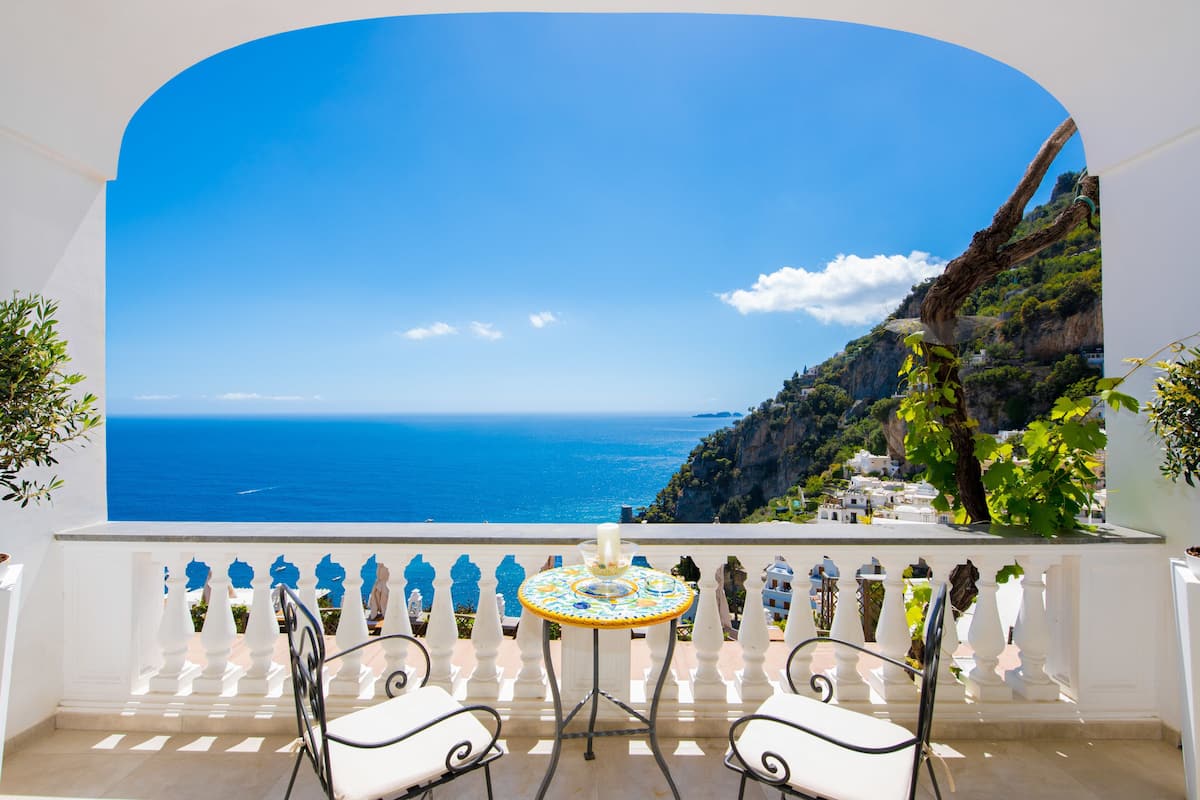 A balcony with a view of the sea, a table, and two chairs.