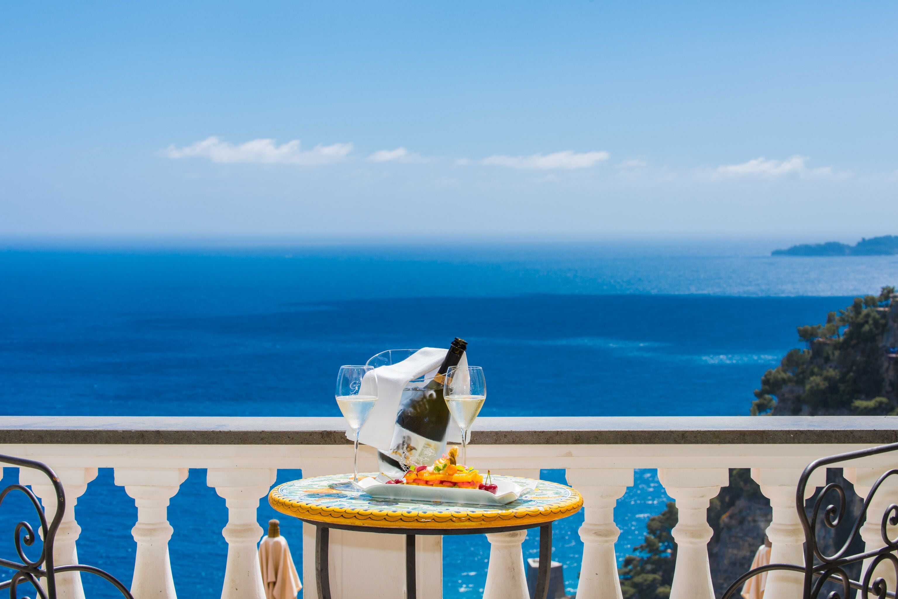 A table with a bottle of champagne and glasses, set against a scenic ocean view.