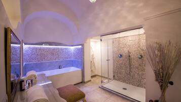 A modern bathroom with a large bathtub, a glass-enclosed shower, and a marble-tiled wall.