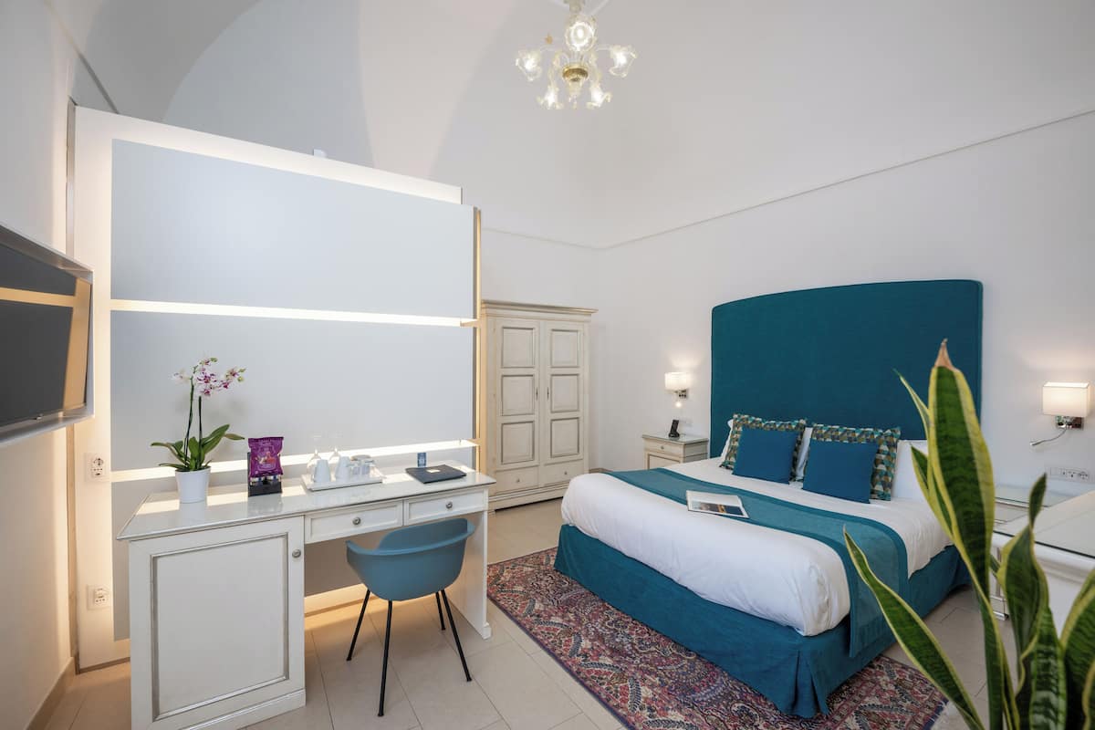 A modern hotel room with a large bed, a desk with a chair, a wardrobe, and a television.