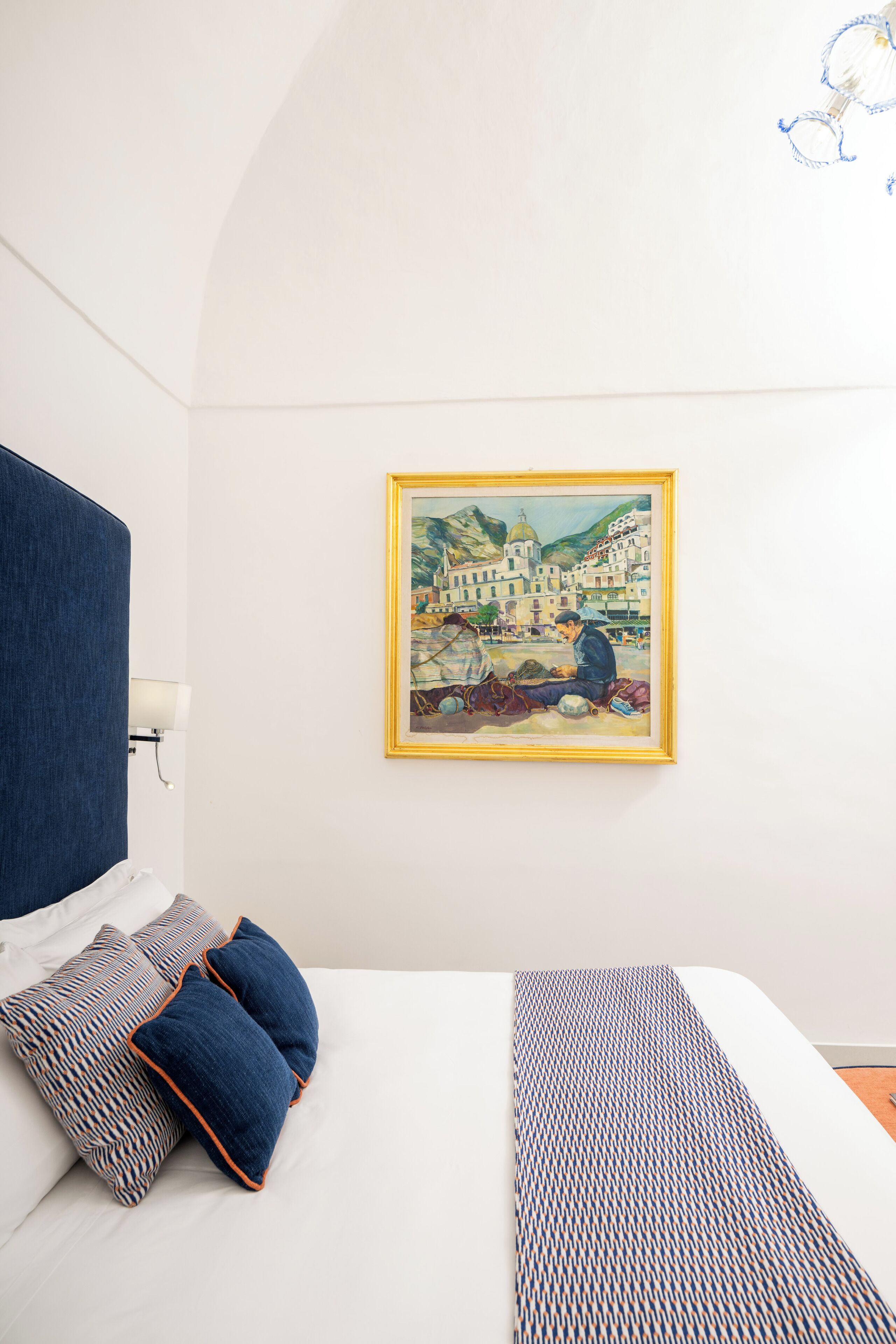 A hotel room with a bed, a painting on the wall, and a blue headboard.