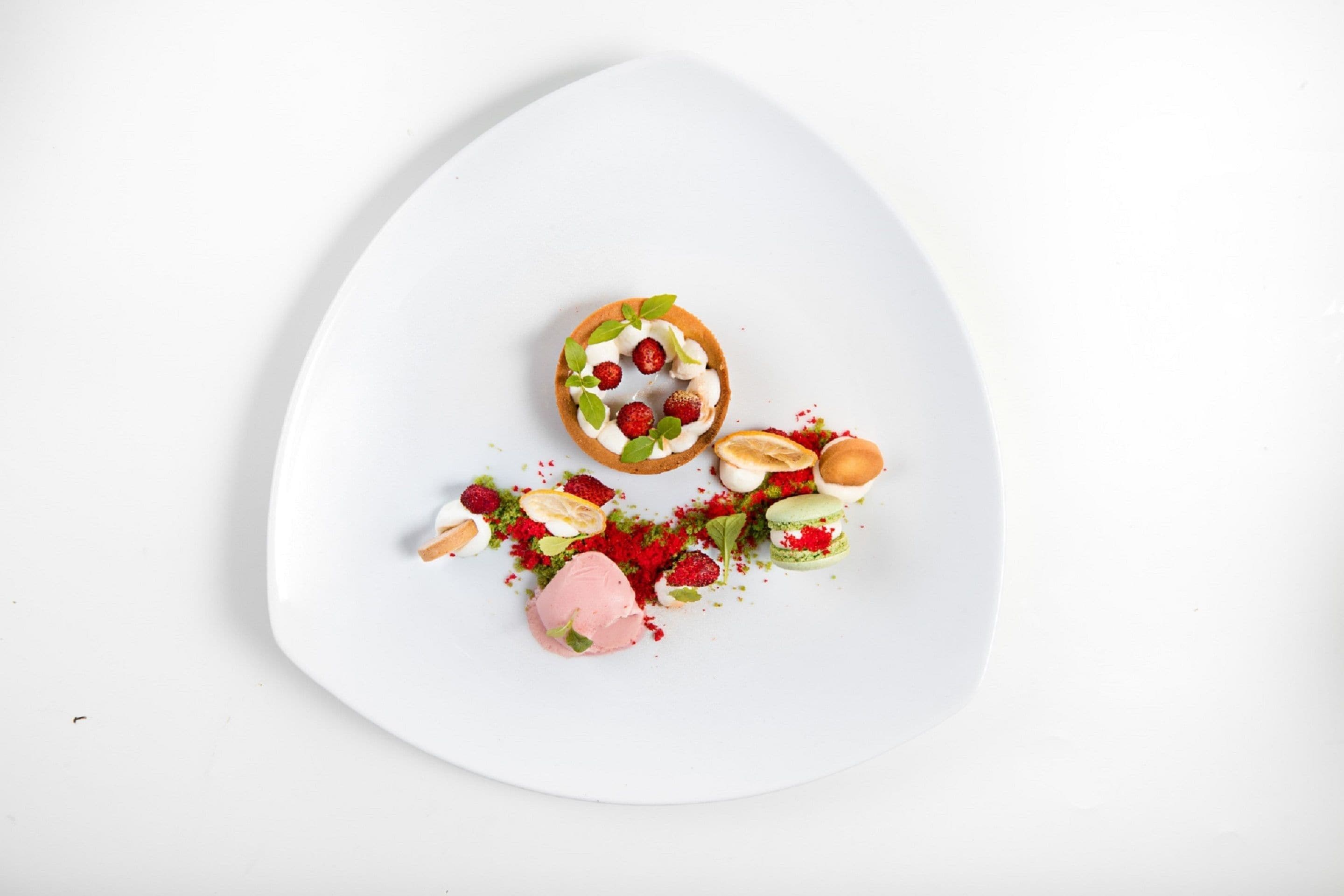 A white plate with a dessert consisting of a tart, strawberries, a scoop of ice cream, and macarons.