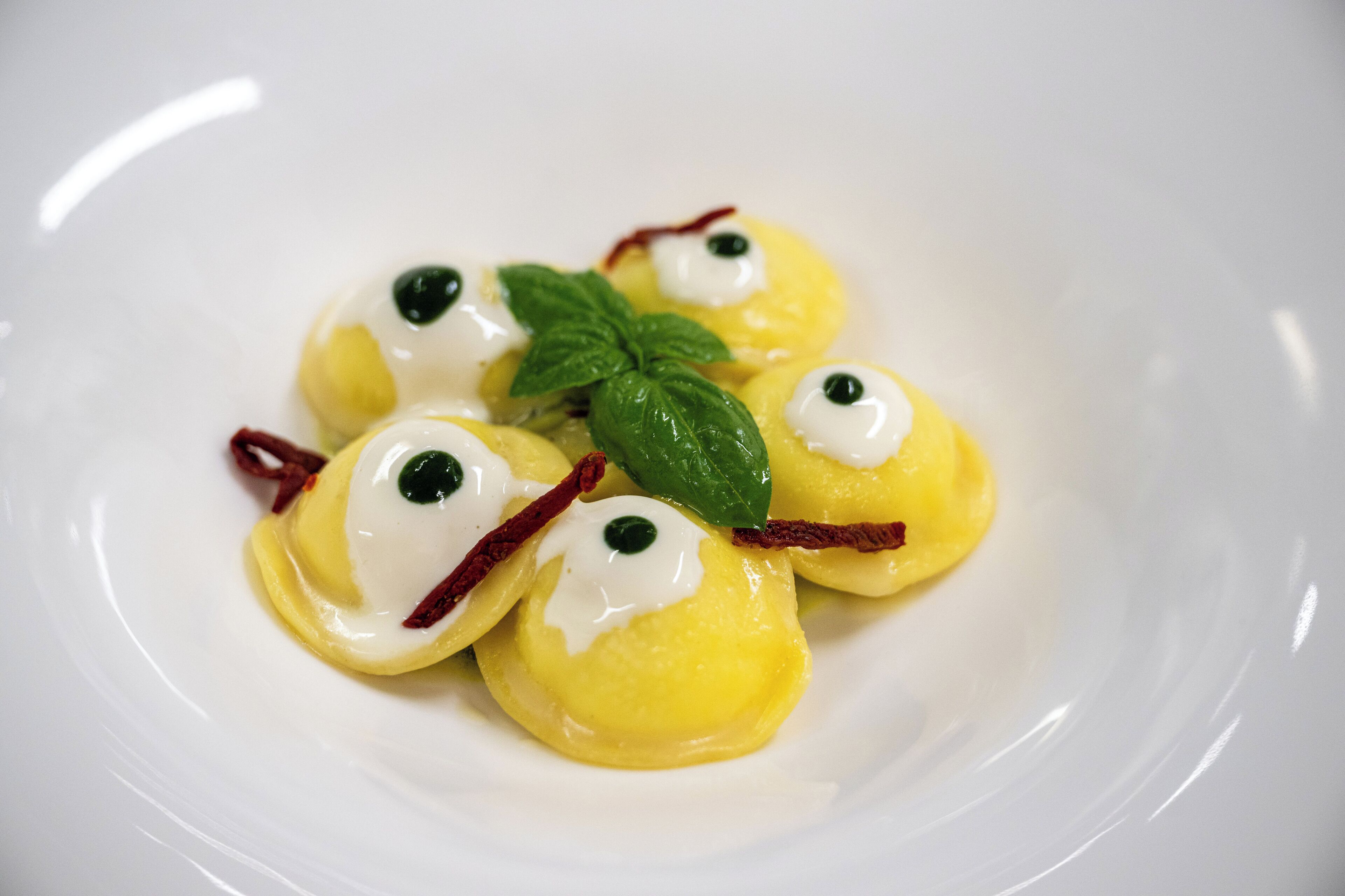 Ein Teller Ravioli mit Sahnehäufchen, garniert mit einem Minzblatt.