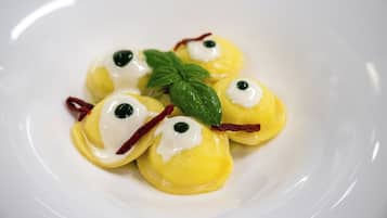 Ein Teller Ravioli mit Sahnehäufchen, garniert mit einem Minzblatt.