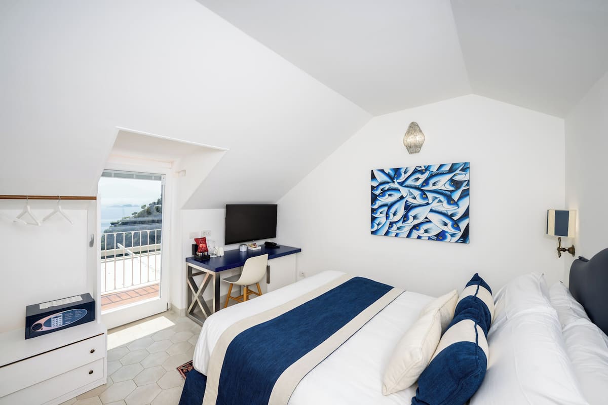 A hotel room with a bed, a desk, a chair, a TV, and a painting on the wall.