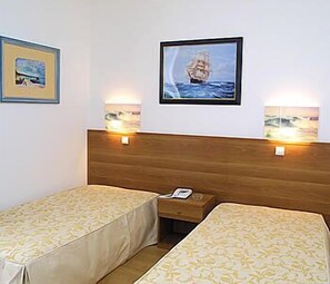 Een hotelkamer met twee eenpersoonsbedden, een houten hoofdbord, twee wandlampen en een ingelijst schilderij boven het hoofdbord.