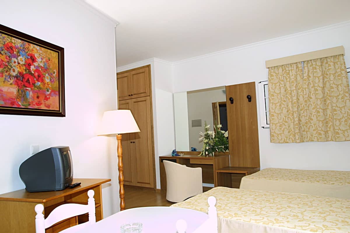 A hotel room with a bed, a desk with a lamp, a television, a mirror, and a painting on the wall.