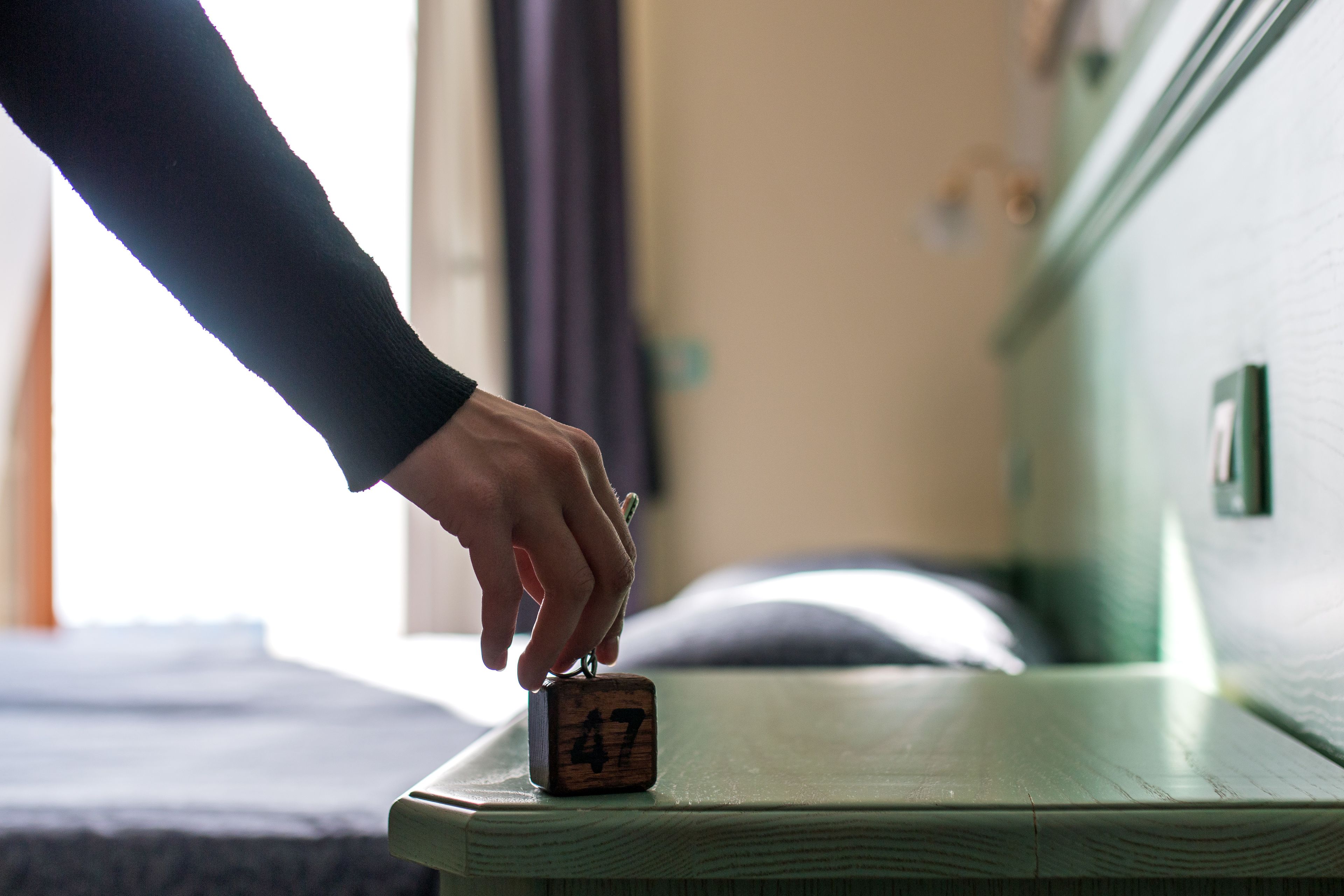 Een hand plaatst een houten blok met het nummer 47 op een houten oppervlak, waarschijnlijk in een hotelkamer.