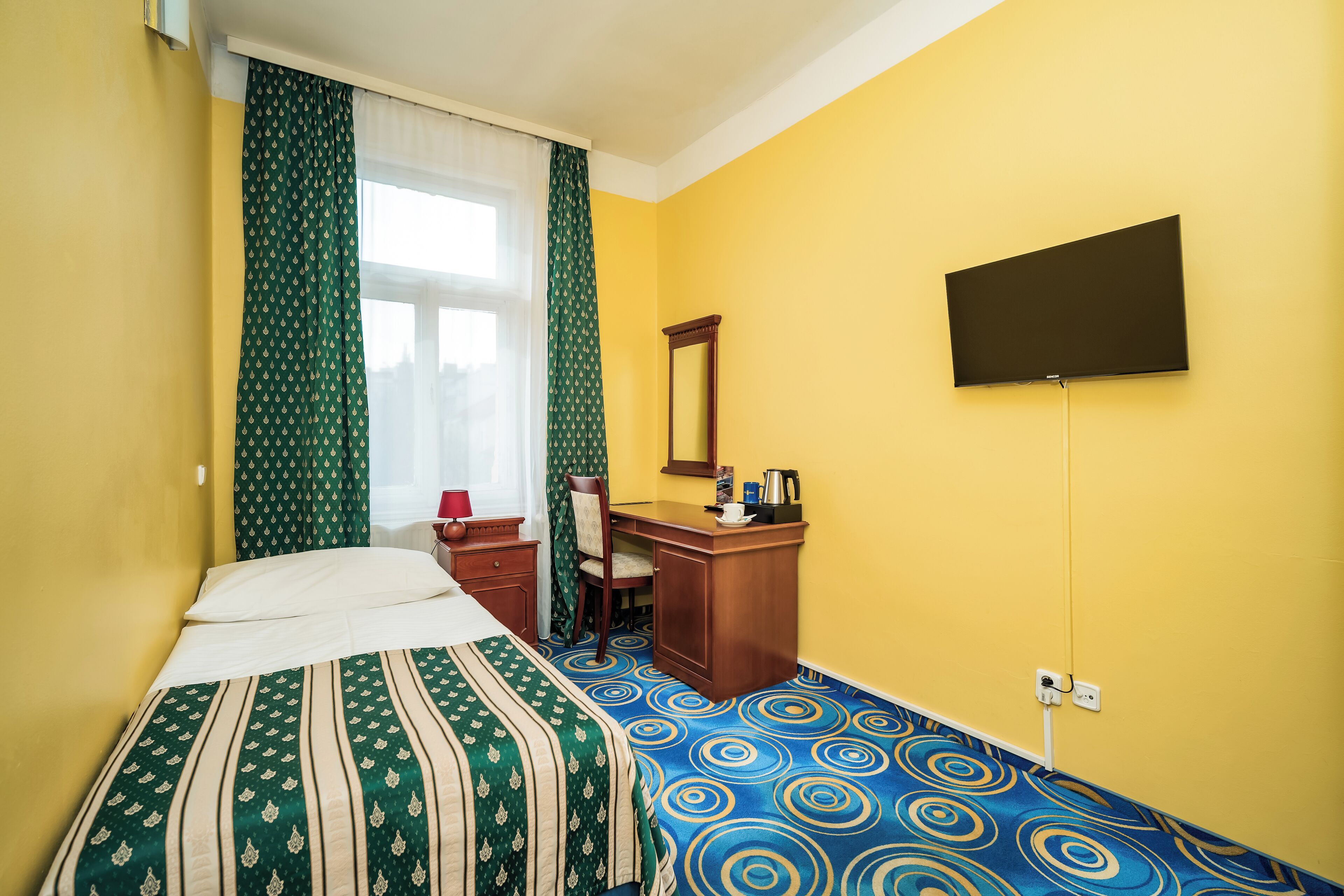A hotel room with a bed, a desk, a chair, a television, and a window with curtains.