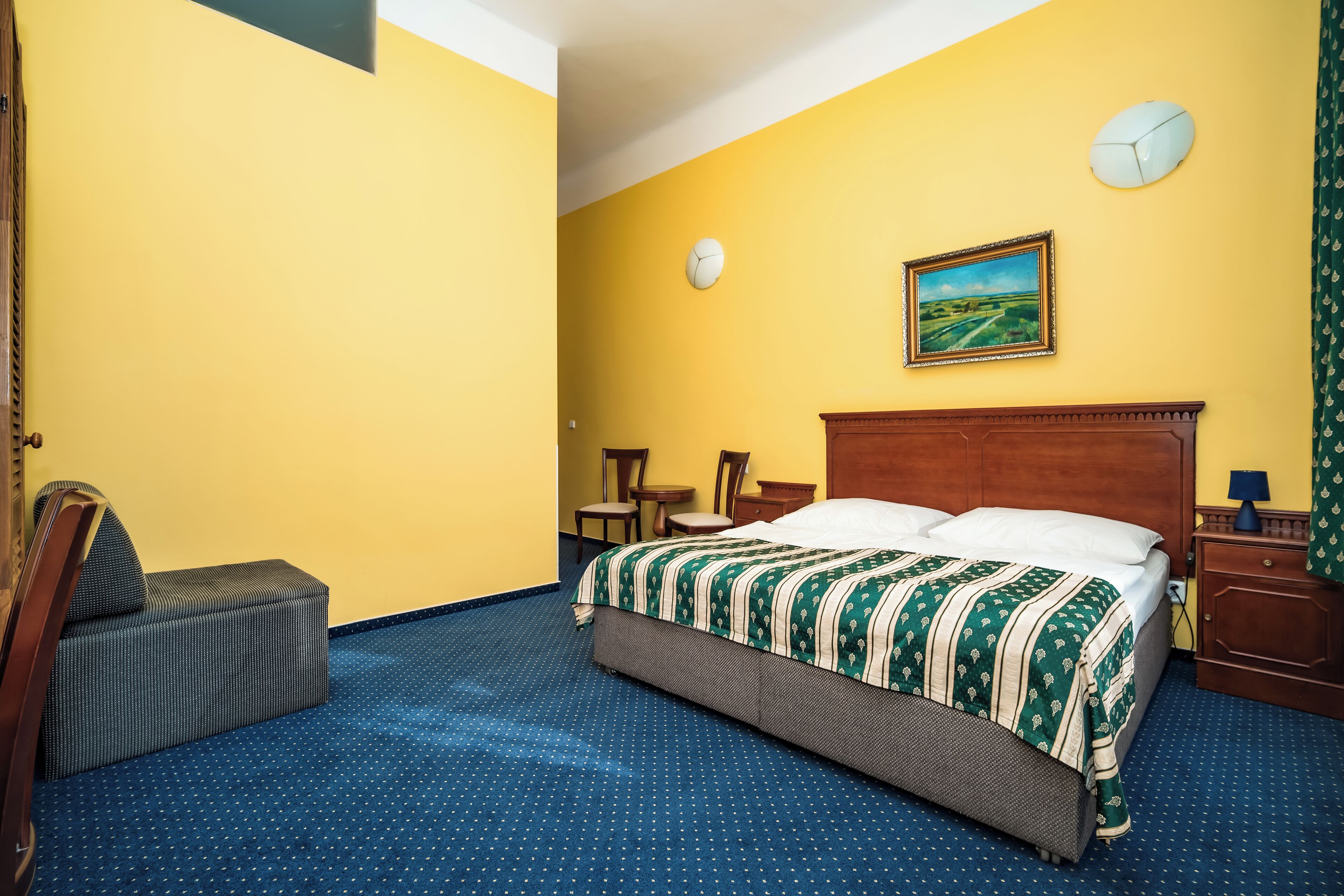 Ein Hotelzimmer mit einem Bett, einem Sessel, einem kleinen Tisch, einer Uhr und einem Bild an der Wand.