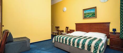 Ein Hotelzimmer mit einem Bett, einem Sessel, einem kleinen Tisch, einer Uhr und einem Bild an der Wand.