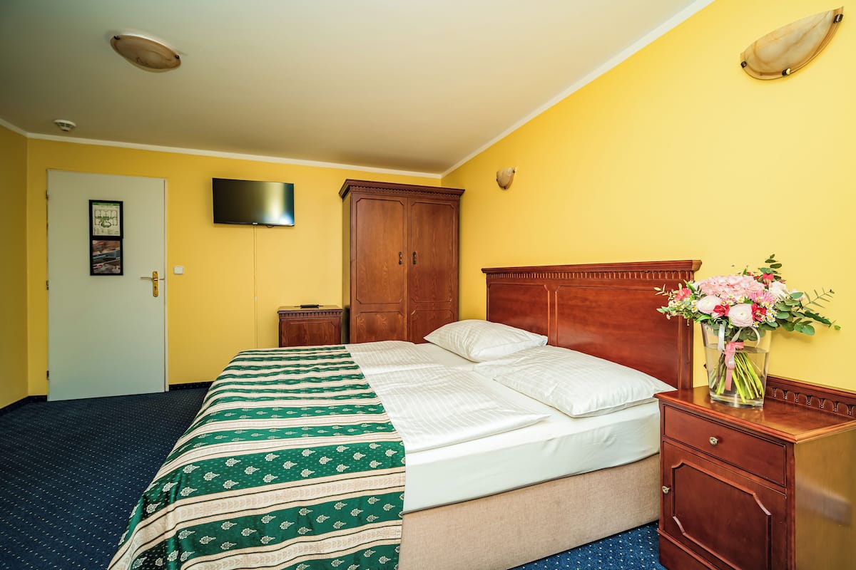 A hotel room with a bed, wooden wardrobe, bedside table, and a TV mounted on the wall.