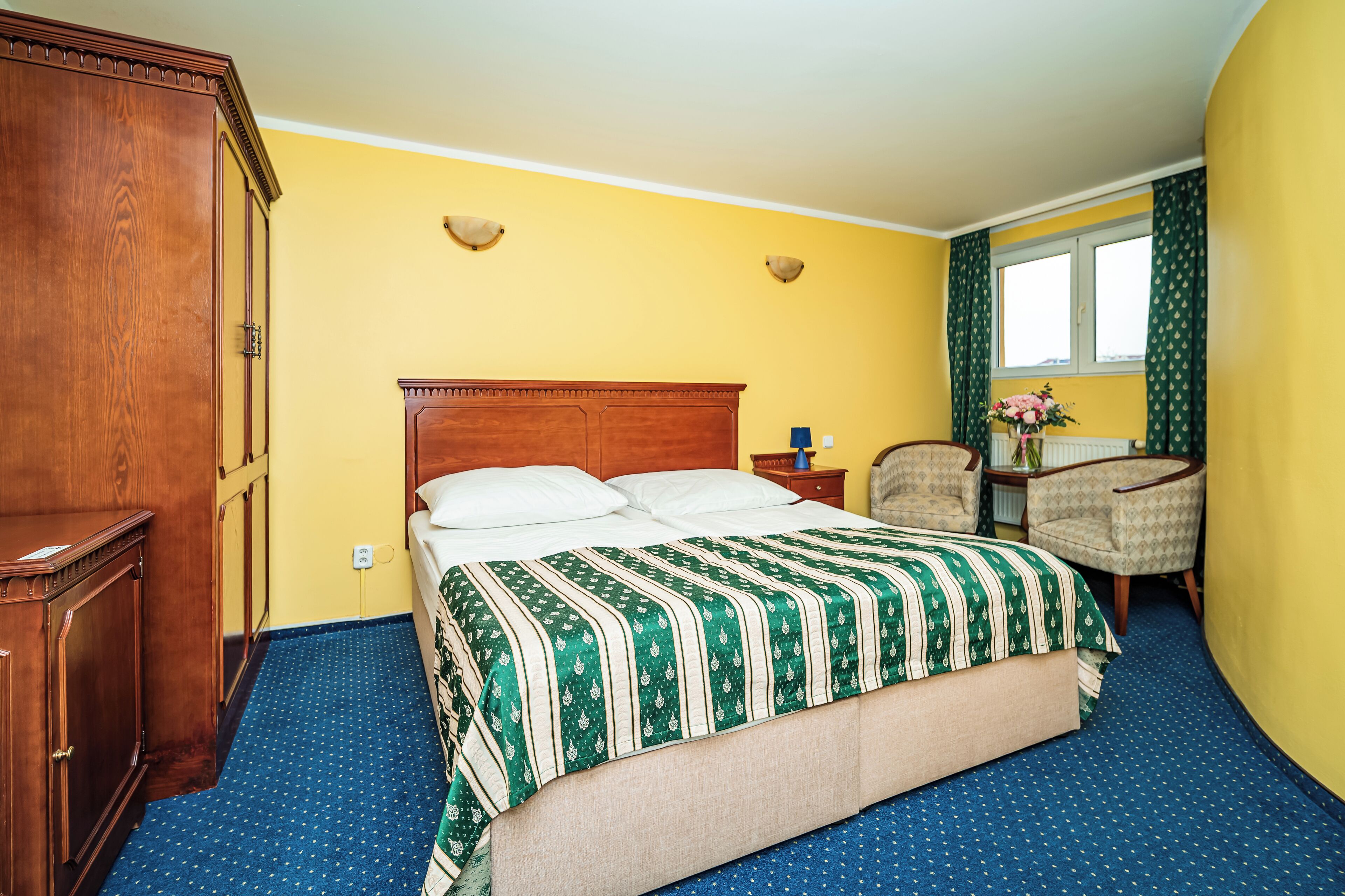 Une chambre d’hôtel avec un grand lit, une armoire en bois, un bureau avec une chaise et une fenêtre avec des rideaux.