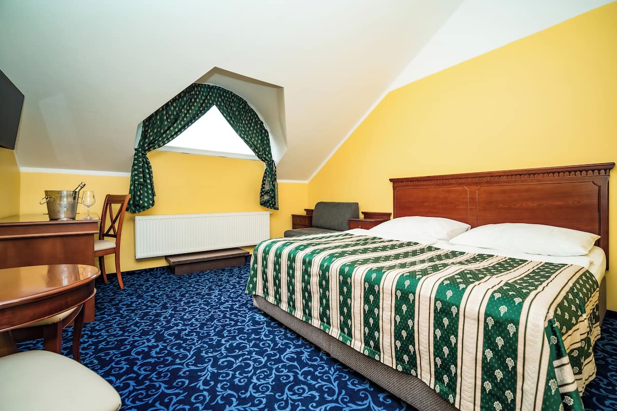 A room with a bed, a desk, a chair, a radiator, and a window with a curtain.