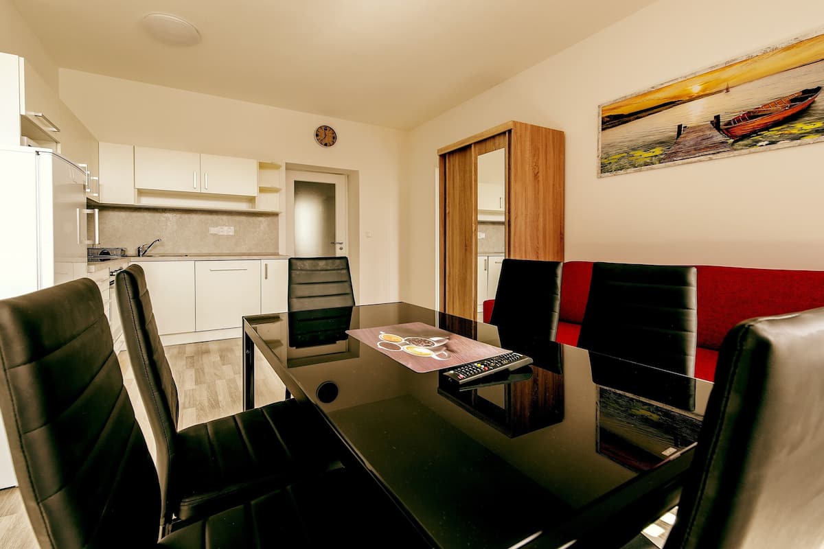 A modern kitchen with white cabinets and a clock on the wall. There is a dining area with a glass table and black chairs.