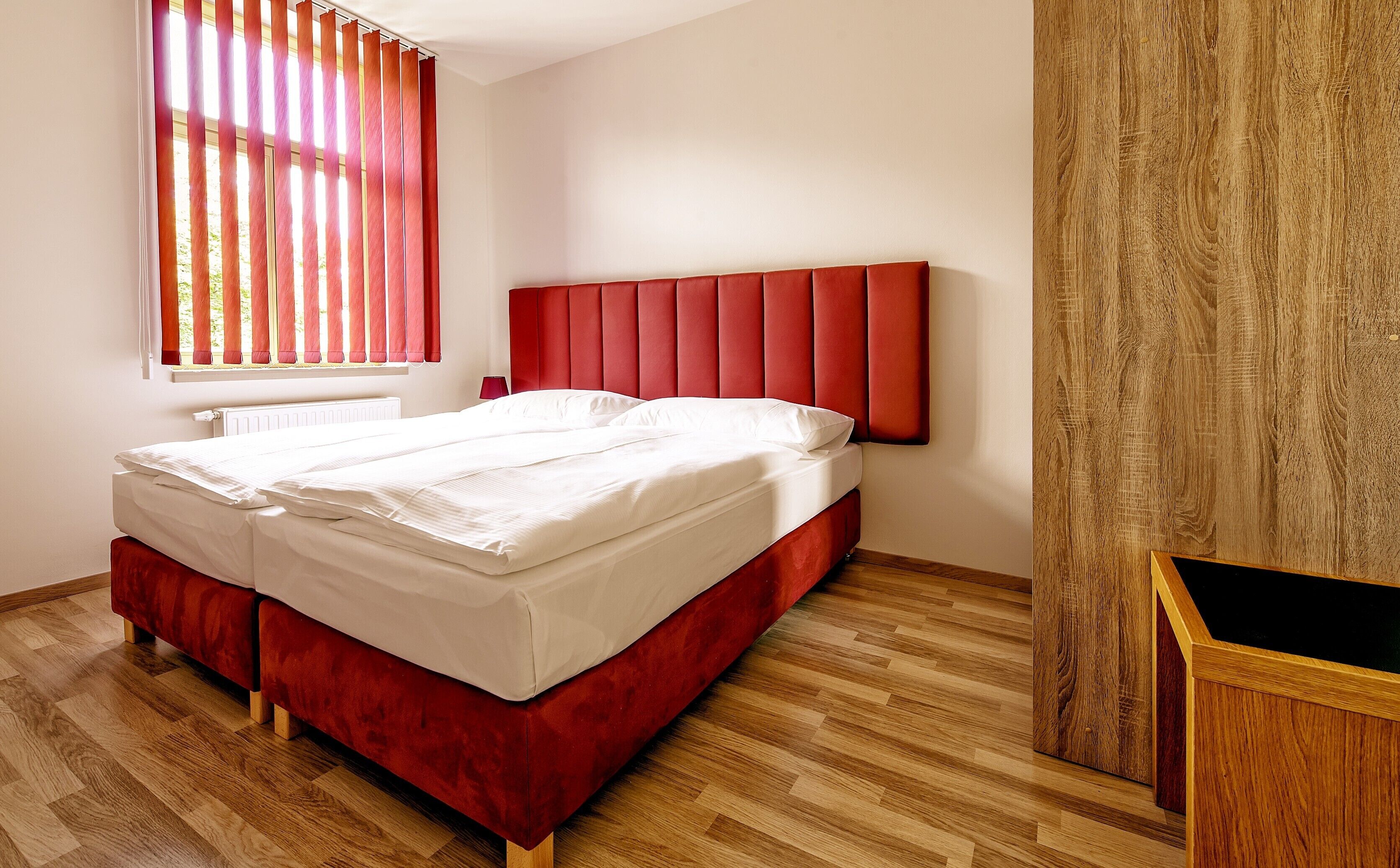 A double bed with a red headboard in a room with wooden flooring.