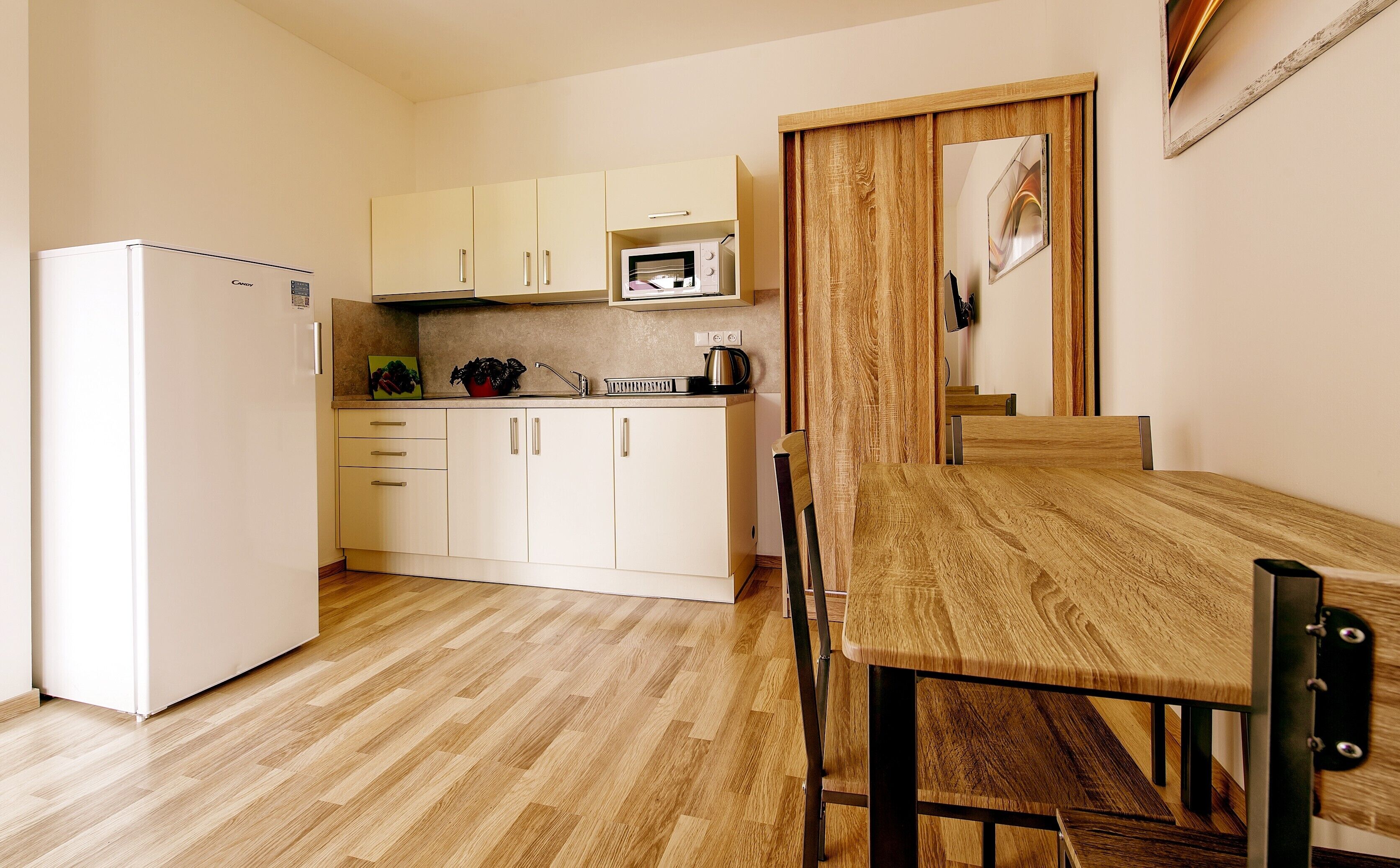A compact kitchen with a refrigerator, microwave, and wooden dining table with chairs.