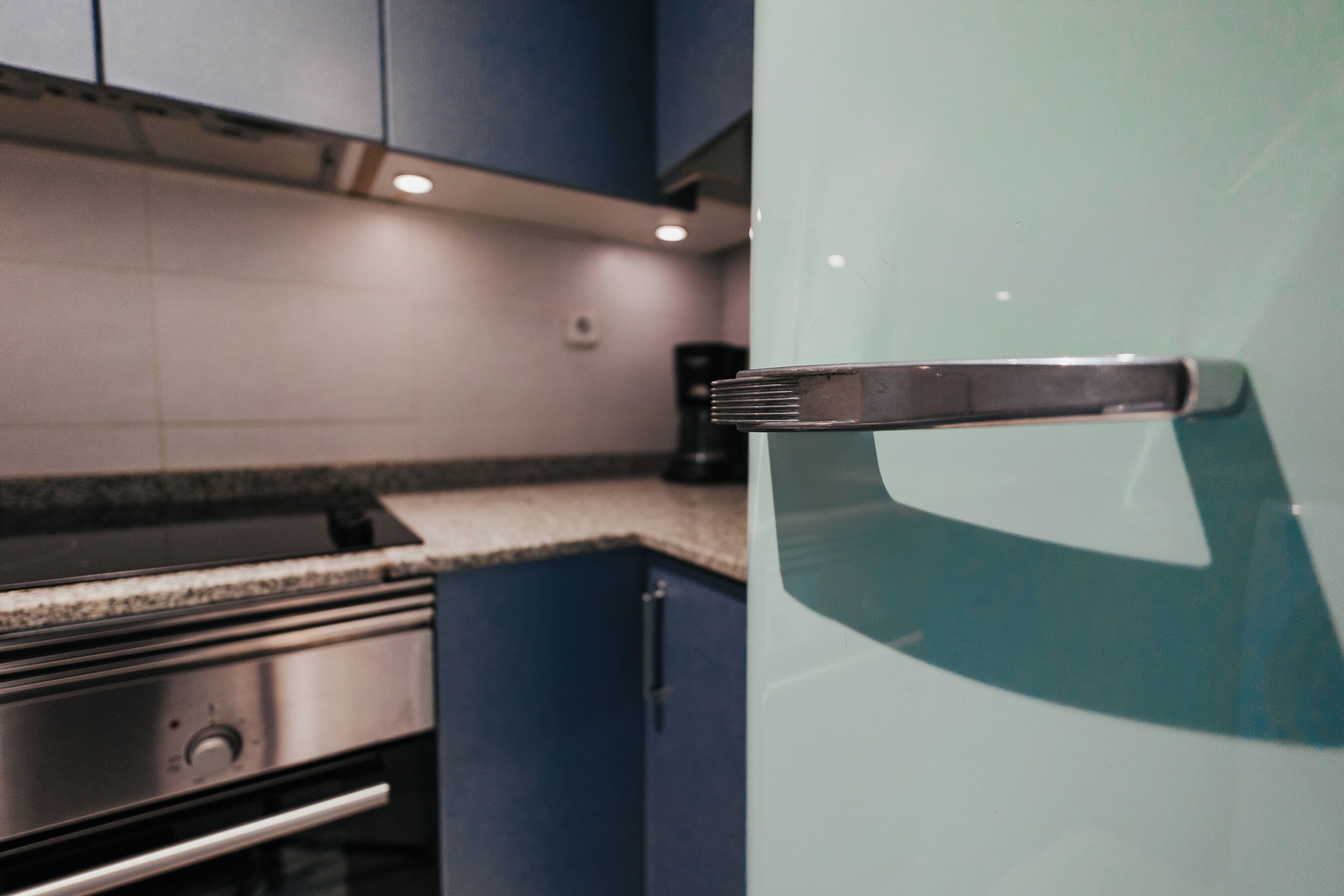 A kitchen with a stainless steel stove, a glass door refrigerator, and blue cabinets.