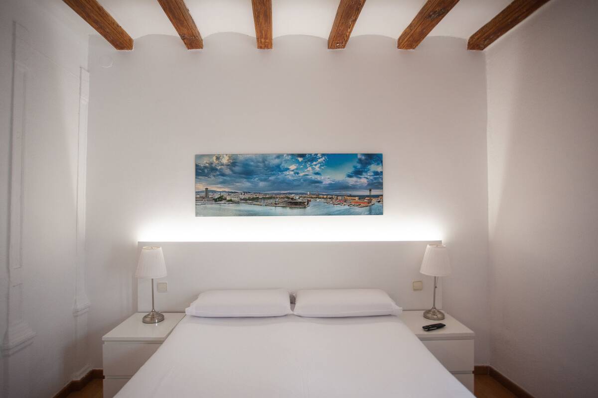 Une chambre d’hôtel avec un lit, deux lampes de chevet, une table de nuit et un tableau représentant un paysage urbain accroché au mur.