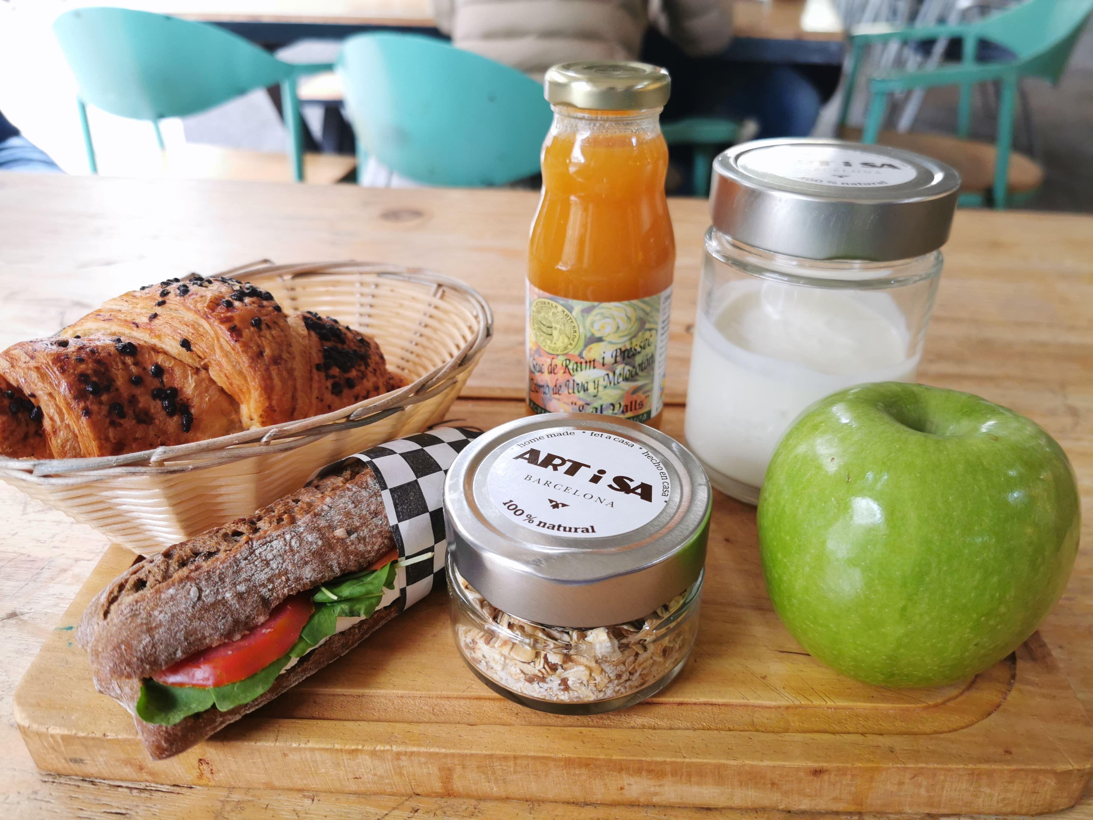 Comida con sándwich, pan, manzana, tarro y botella sobre una mesa de madera.