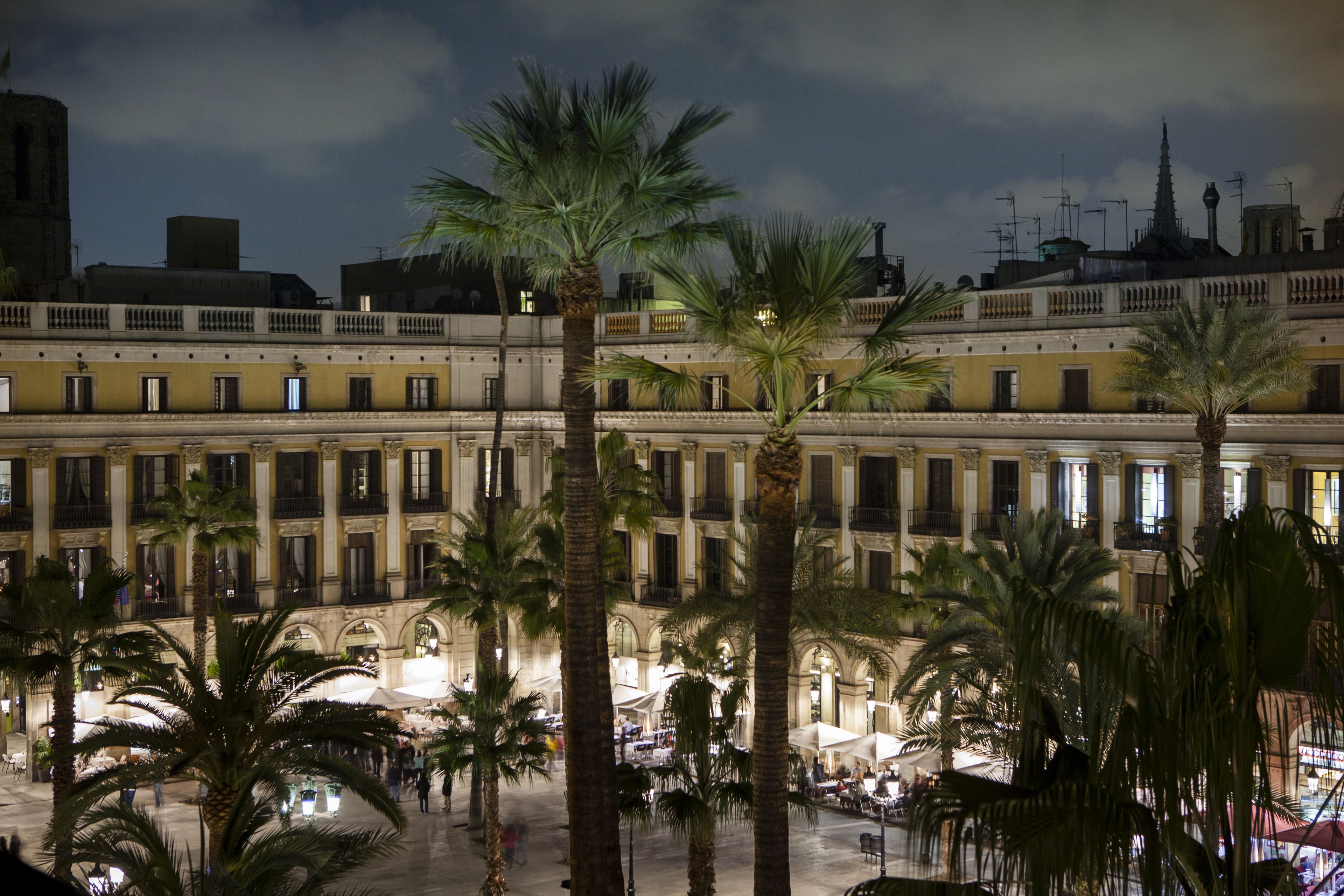 A historic building with multiple floors, large windows, and a courtyard with palm trees.