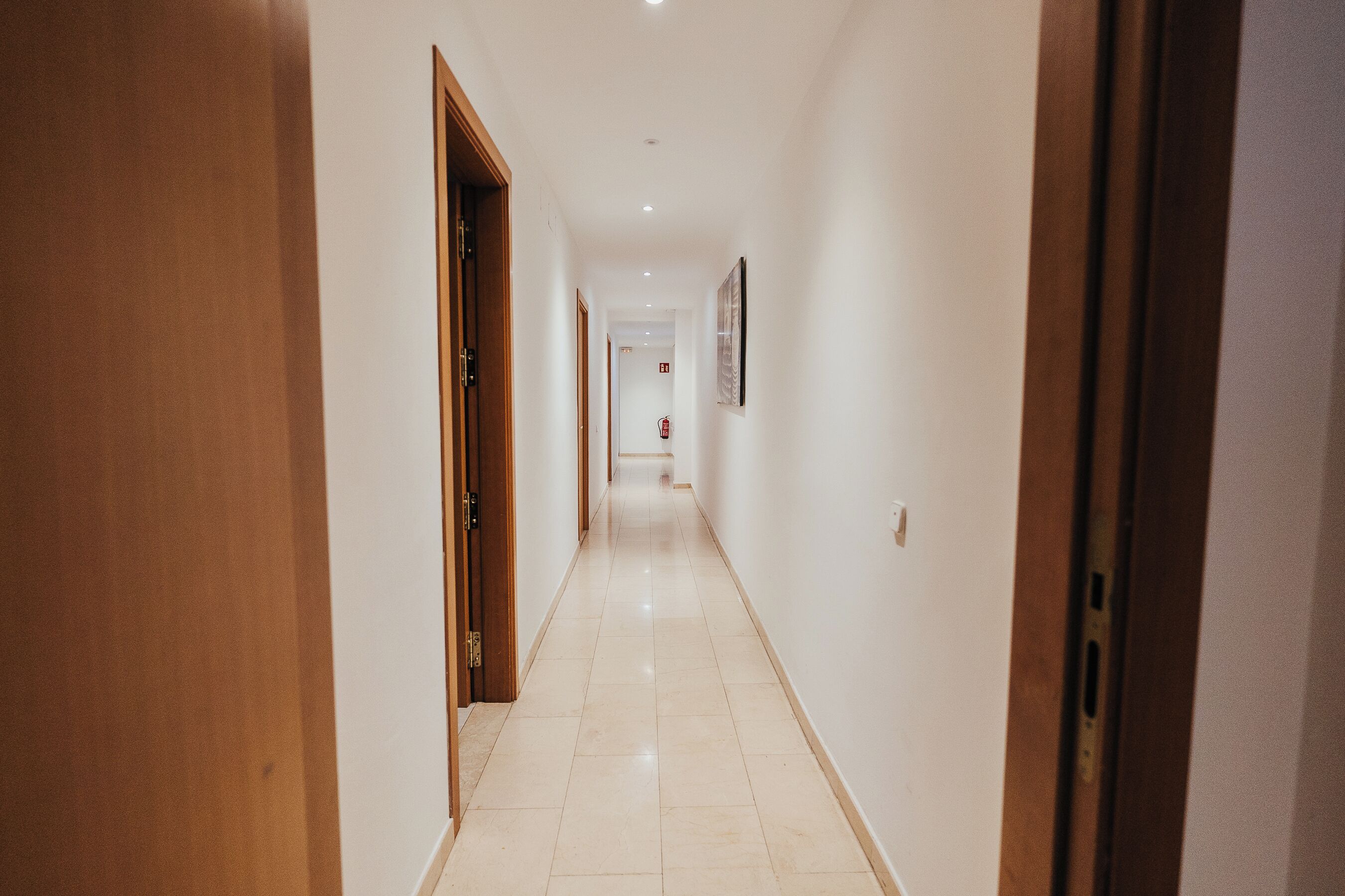 A corridor with wooden doors on one side and a white wall on the other.