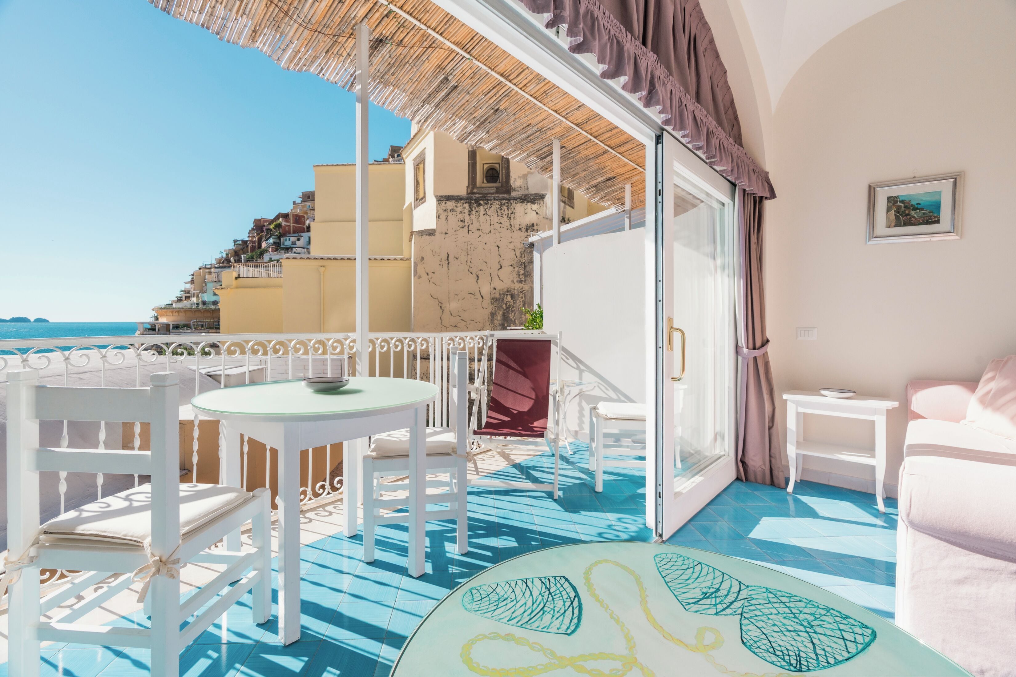 Un balcon avec des chaises blanches et une table, une vue sur la mer et un immeuble doté d’un escalier.