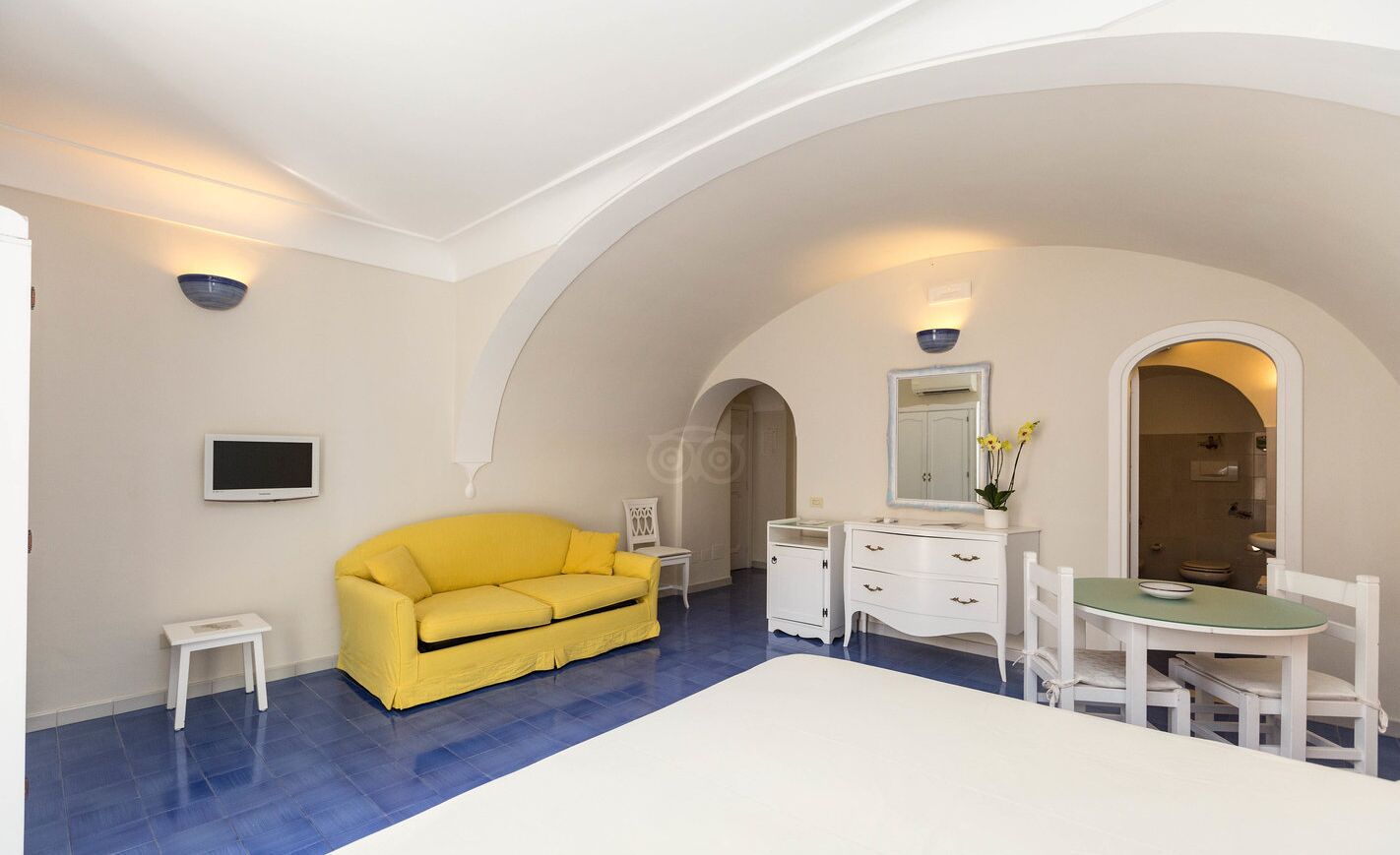 Une chambre avec un canapé jaune, une commode blanche, une petite table et une chaise verte.