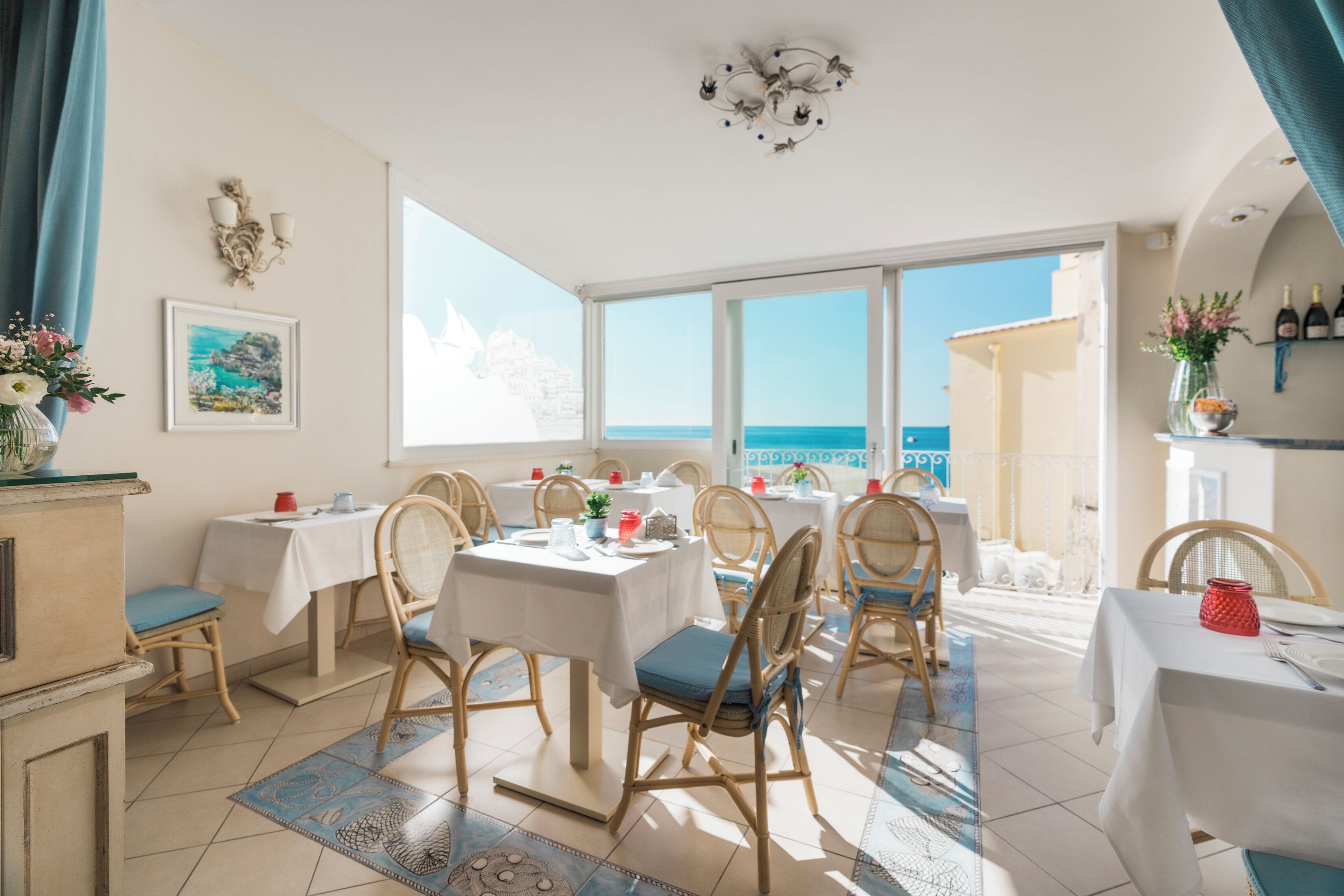 A dining area with tables and chairs, a view of the sea, and a chandelier.