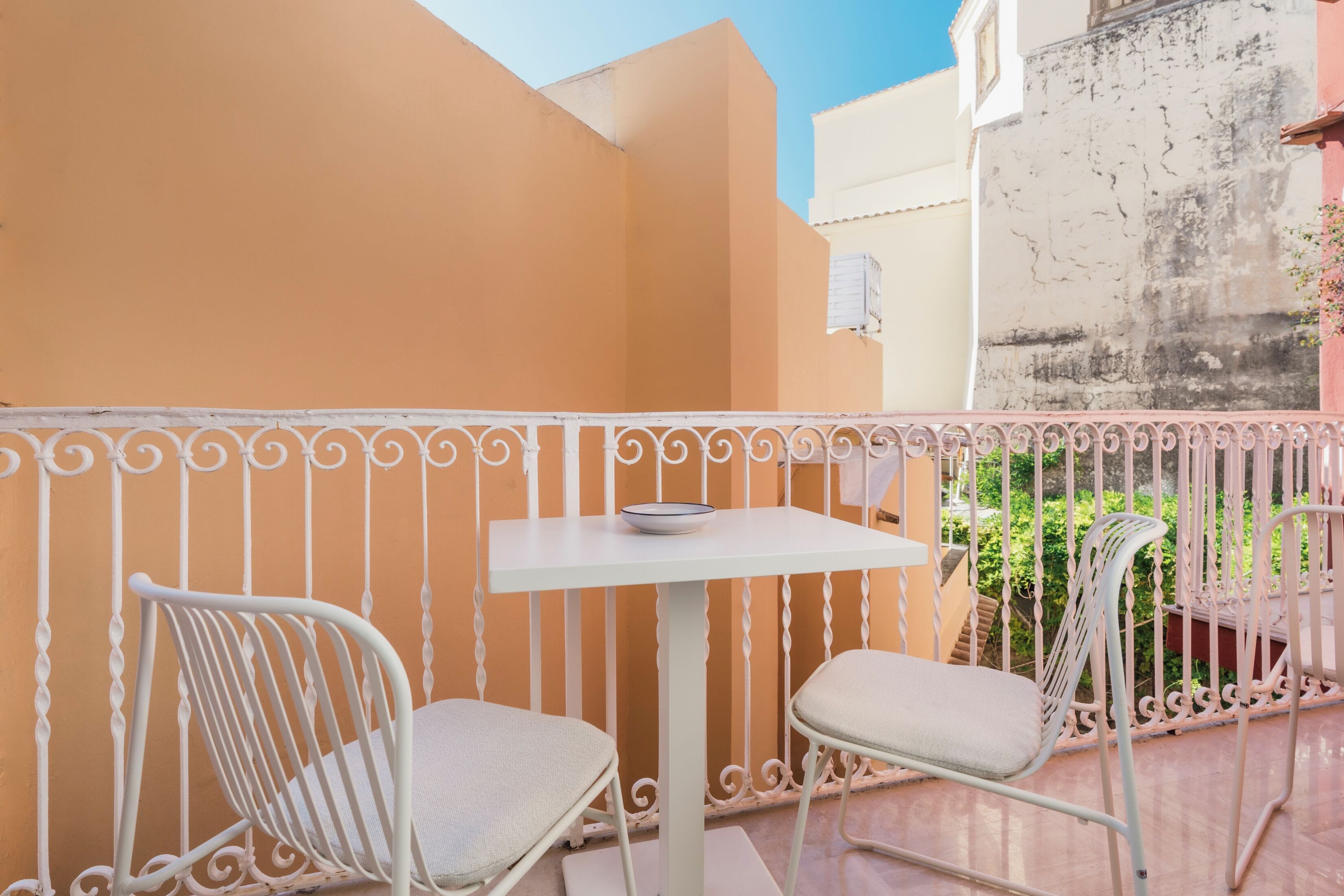 A balcony with two white metal chairs and a small table, surrounded by a white wrought iron railing.