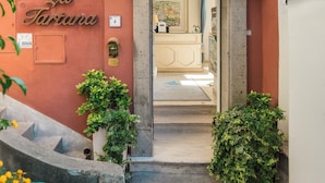 La entrada de Villa La Tartana, con un balcón de hierro forjado, un cartel sobre la puerta y un pequeño jardín con plantas y flores.