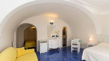 A hotel room with a bed, a desk, a chair, and a small table. There is a mirror above the desk and a window with a view of the outside.