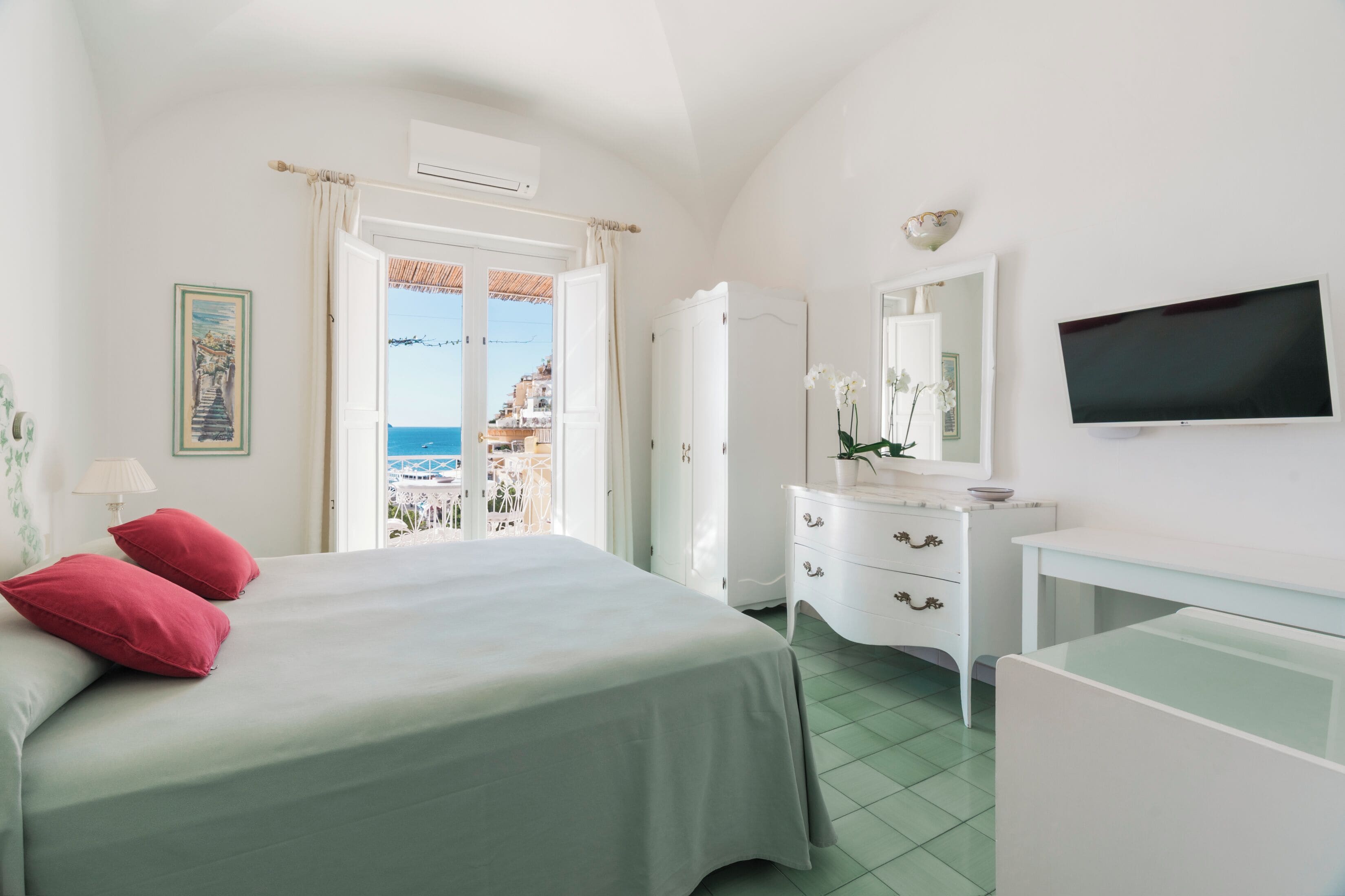 A bedroom with a bed, a dresser, a TV, and a view of the sea.