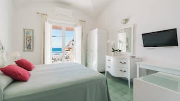 A bedroom with a bed, a dresser, a TV, and a view of the sea.