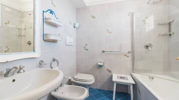 A bathroom with a large sink, bidet, toilet, and a shower area.