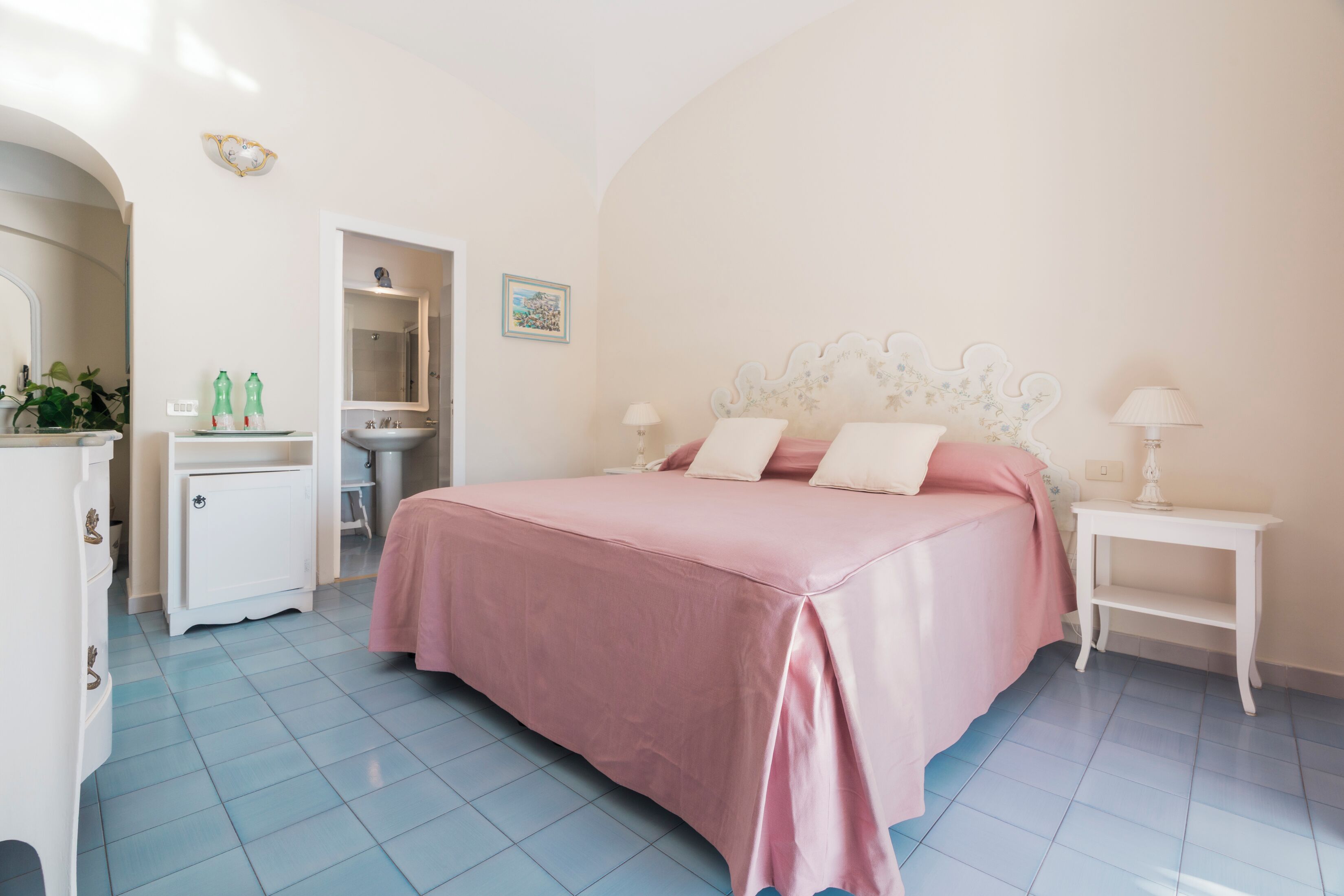 Une chambre à coucher avec un lit, des tables de chevet, une commode et une salle de bain visible à travers une porte ouverte.