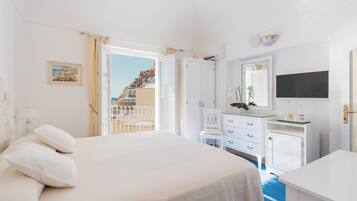 A hotel room with a bed, a desk, a dresser, and a view of a coastal town.