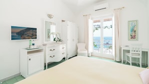Un dormitorio con cama, cómoda, silla, escritorio y balcón con vista al mar.