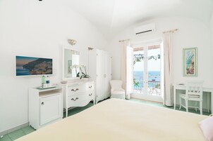 Un dormitorio con cama, cómoda, silla, escritorio y balcón con vista al mar.