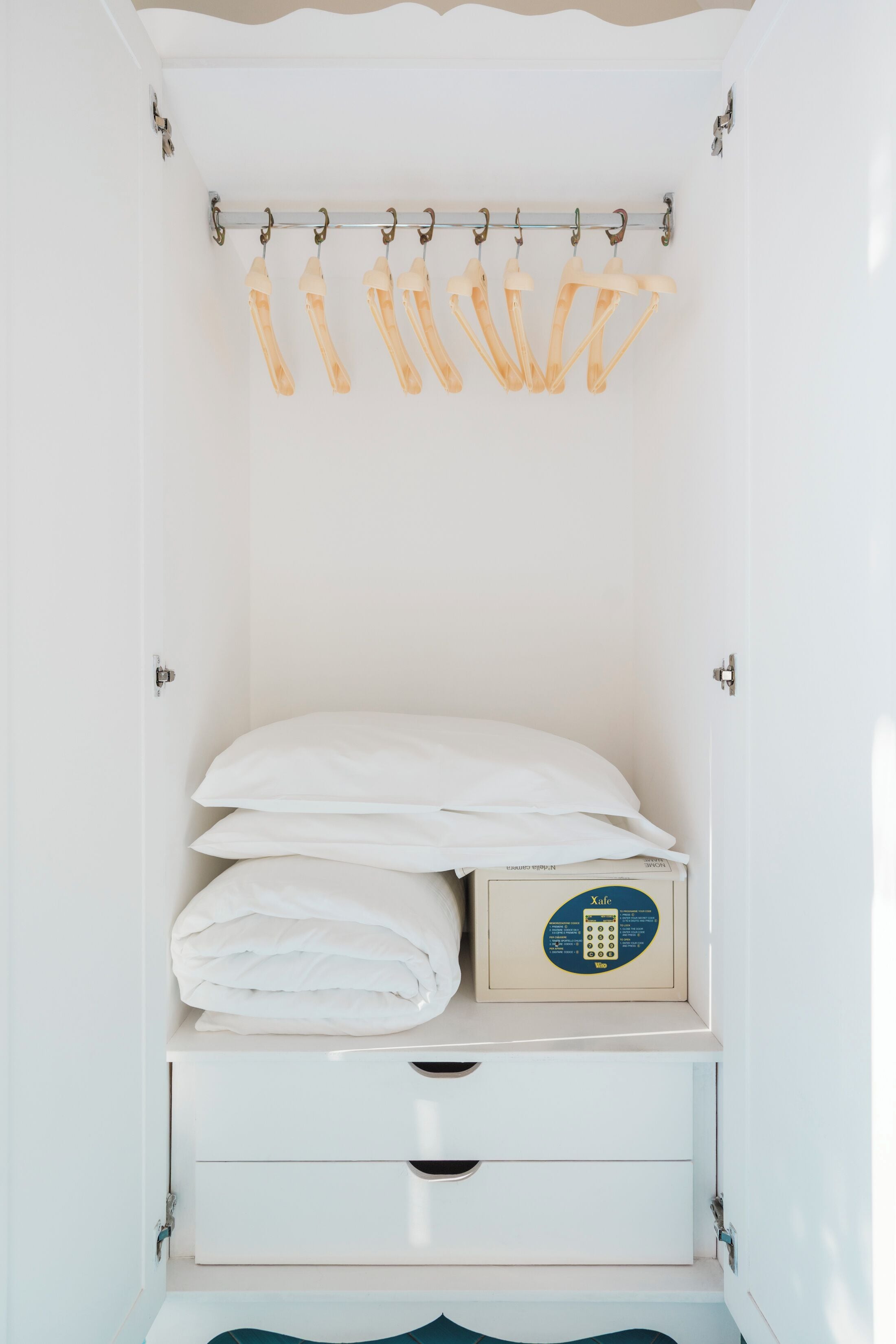 Ein weißer Kleiderschrank mit Kleiderstange, einem ausgeklappten Bett und einer kleinen Kommode.