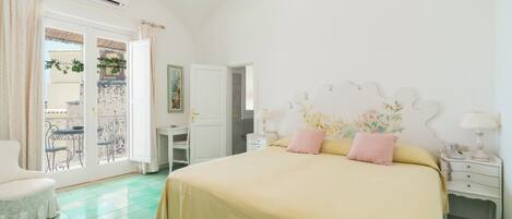 A bedroom with a large bed, a desk, a chair, and a balcony with a table and chairs.