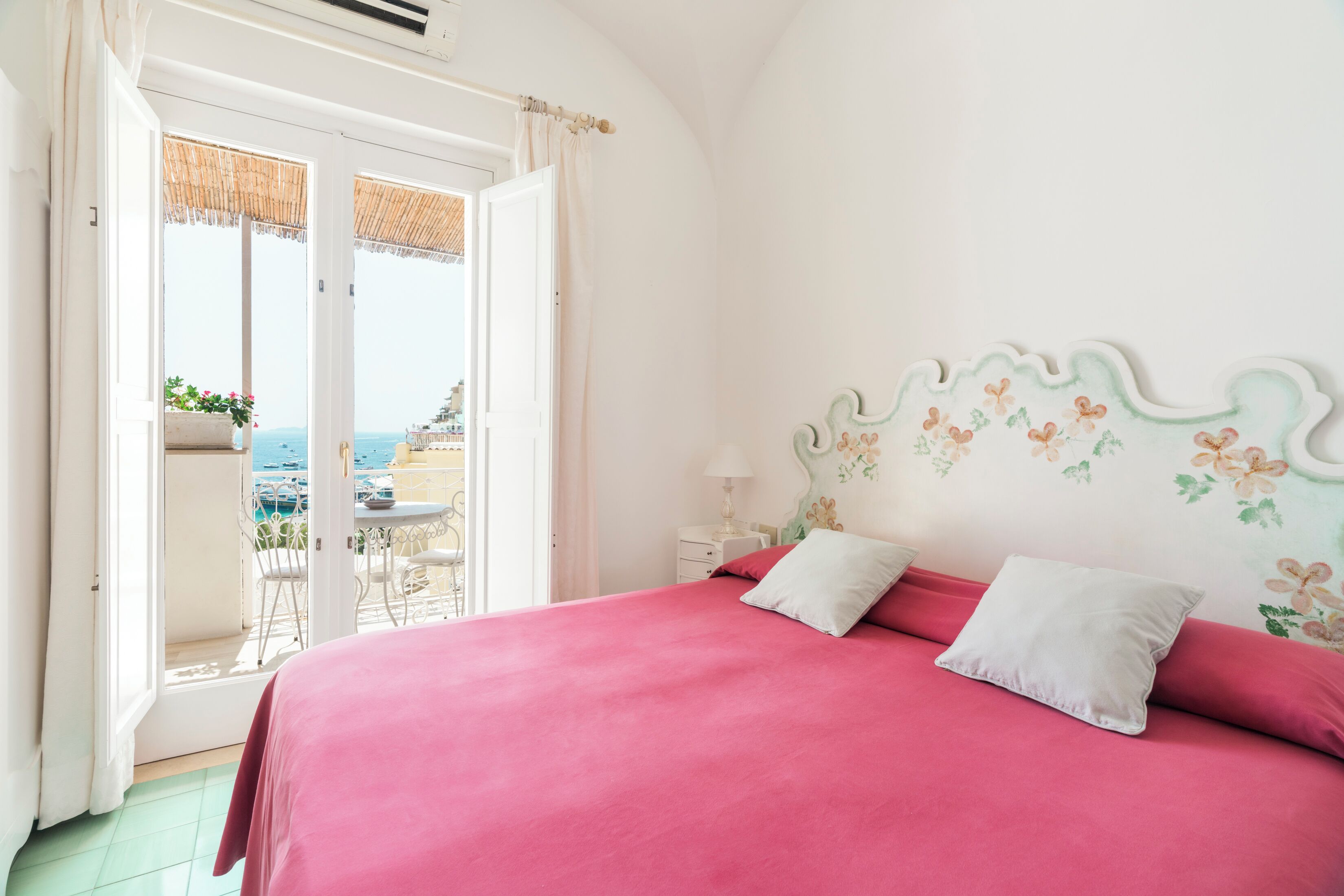 Un dormitorio con una cama grande, un balcón con vistas al mar y una pequeña mesa con sillas.