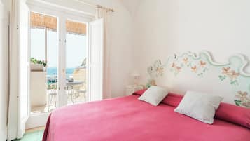 Un dormitorio con una cama grande, un balcón con vistas al mar y una pequeña mesa con sillas.